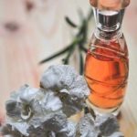 Glass perfume bottle alongside dew-kissed white carnation flowers on wood surface.